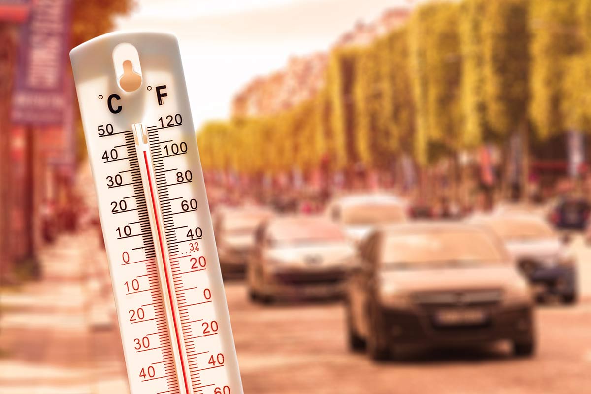 Im Vordergrund steht ein Thermometer, das 40 Grad anzeigt. Im Hintergrund ist eine Straße voller Autos zu sehen