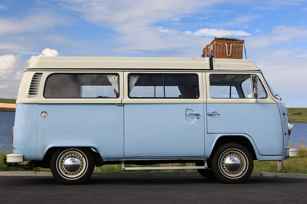 Ein blauer VW Bulli steht vor einem See