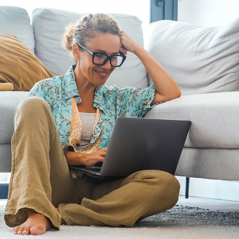 Eine Frau guckt auf einen Laptop und lächelt
