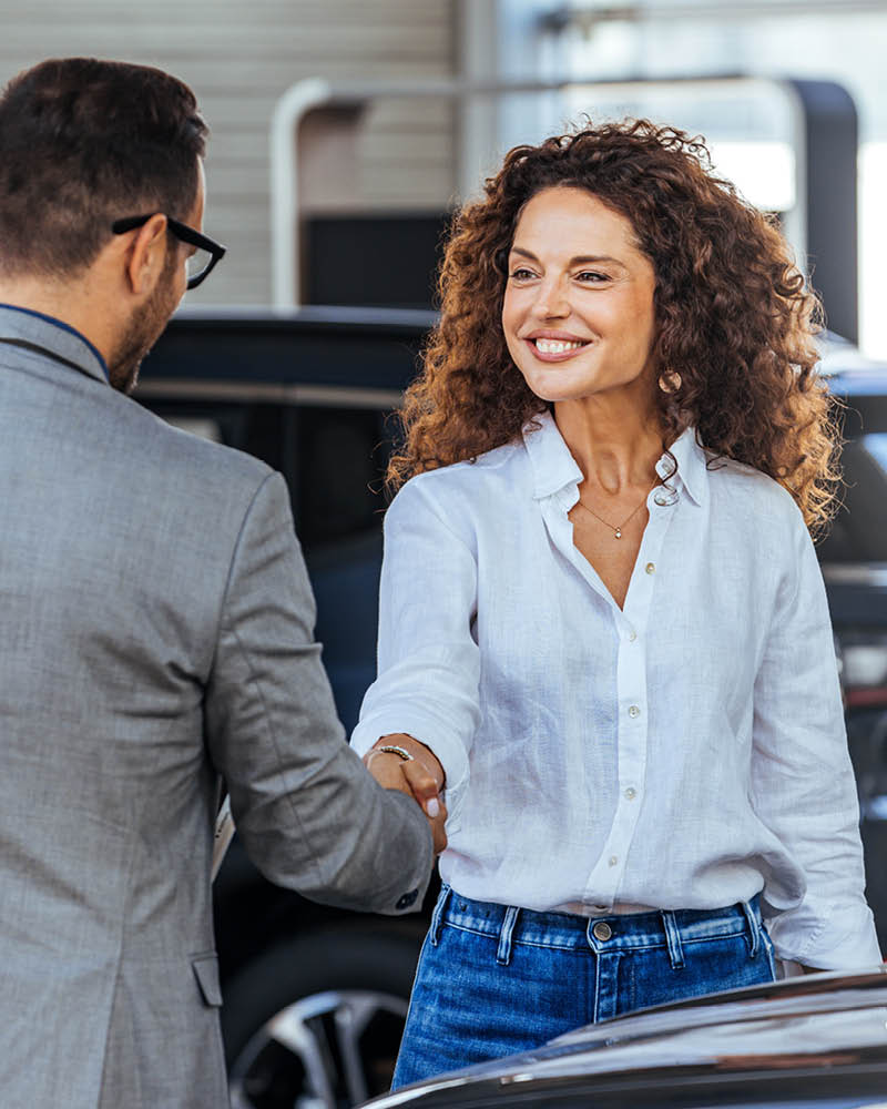 Autoverkäufer und Kundin geben sich die Hände und lächeln dabei
