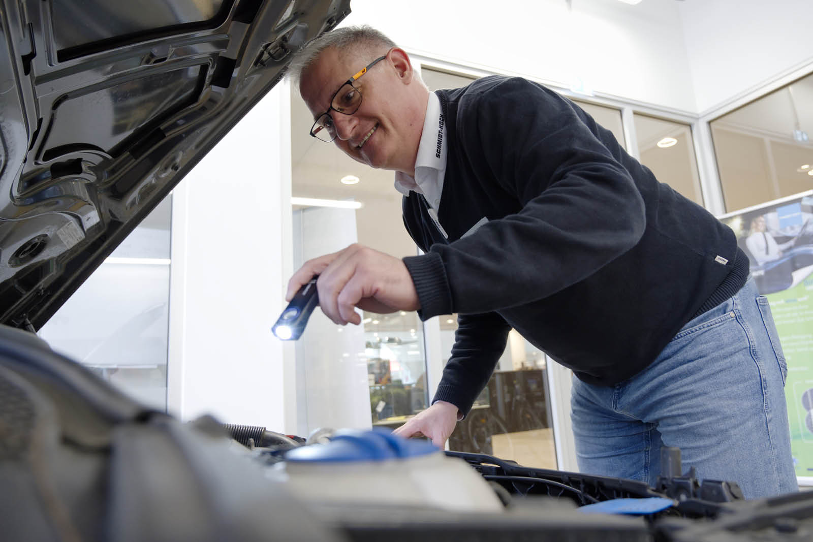 Mitarbeiter vom Autohaus leuchtet in eine Motorhaube